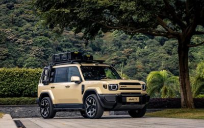 Photographie d'un SUV iCAUR beige, modèle V27, sur un parking pavé, avec une montagne verdoyante en arrière-plan.
